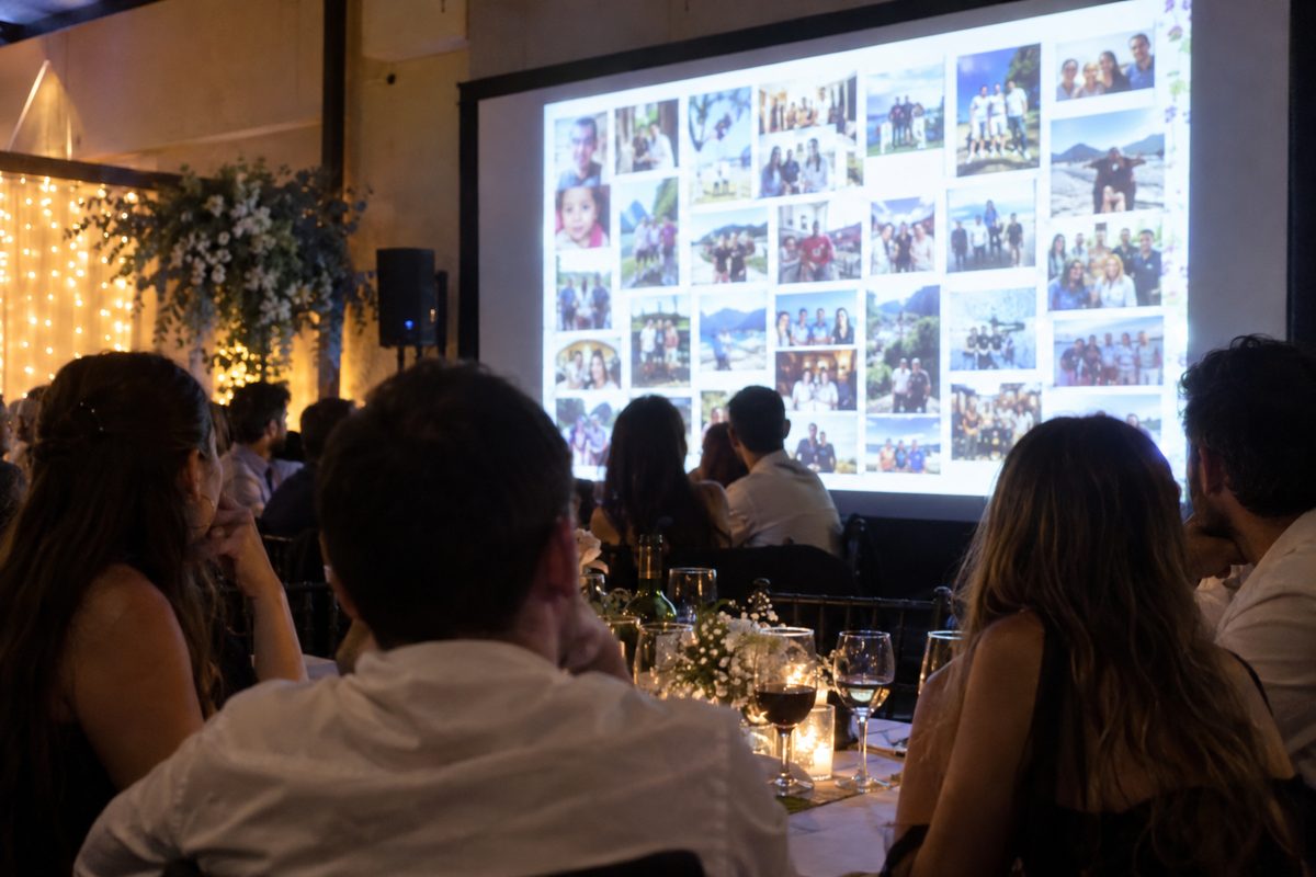 Los invitados miran la pantalla del salón, que muestra un mosaico con las fotos del evento