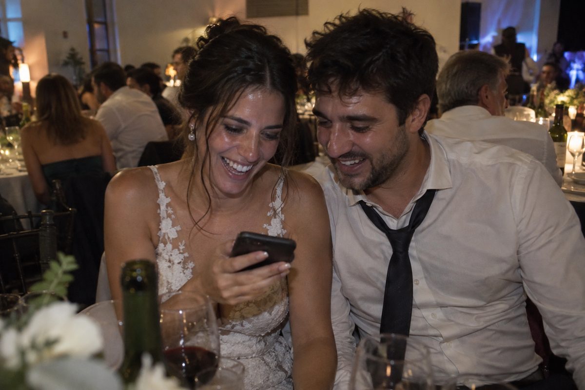 Los novios se ríen mirando juntos en el celular las fotos que subieron los invitados
