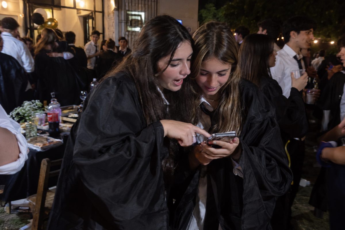 Dos compañeras de egreso escolar miran juntas las fotos en el celular